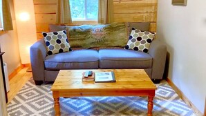 A cozy room with a wooden wall, a grey sofa with patterned cushions, a wooden coffee table, and a patterned rug. - Log Cabin in North Georgia Mountains (Dahlonega)