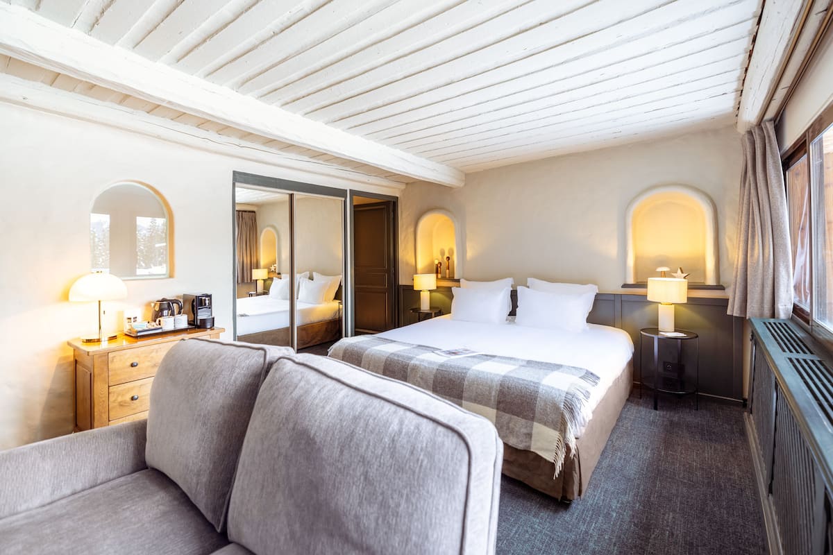 A hotel room with a bed, two bedside tables with lamps, a sofa, a mirror, and a window with curtains.