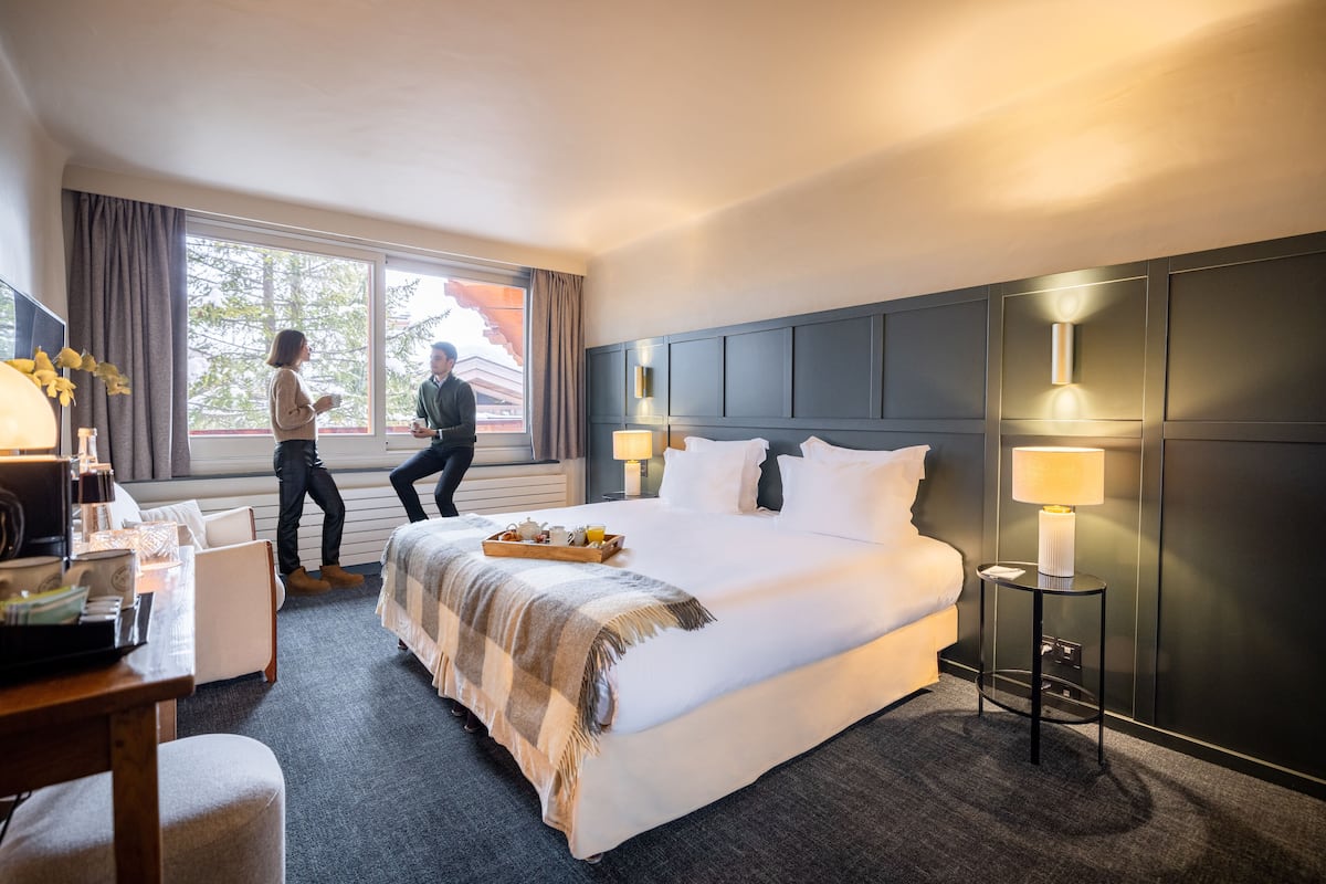 A hotel room with a large bed, bedside lamps, a desk with a chair, and a window with curtains.