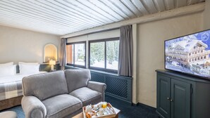 Habitación de hotel con sofá, una mesa de comedor con desayuno, televisor y ventana con vista a un edificio.