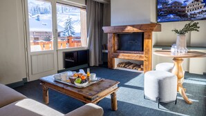 Una sala de estar acogedora con chimenea, una mesa de comedor con desayuno y un amplio ventanal con vistas a una montaña nevada.