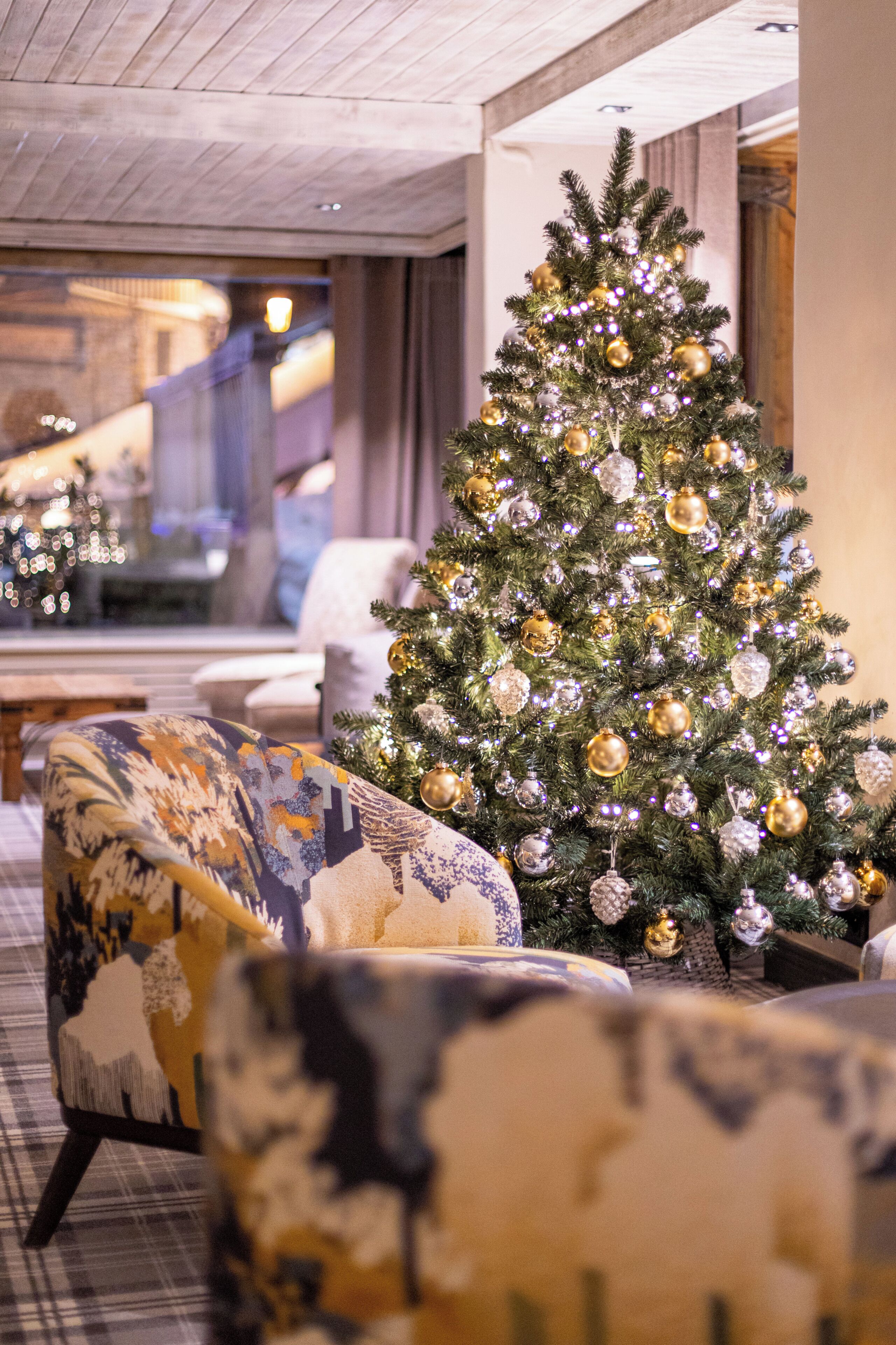 Ein Weihnachtsbaum mit Verzierungen, ein gemustertes Sessel und eine Treppe im Hintergrund.