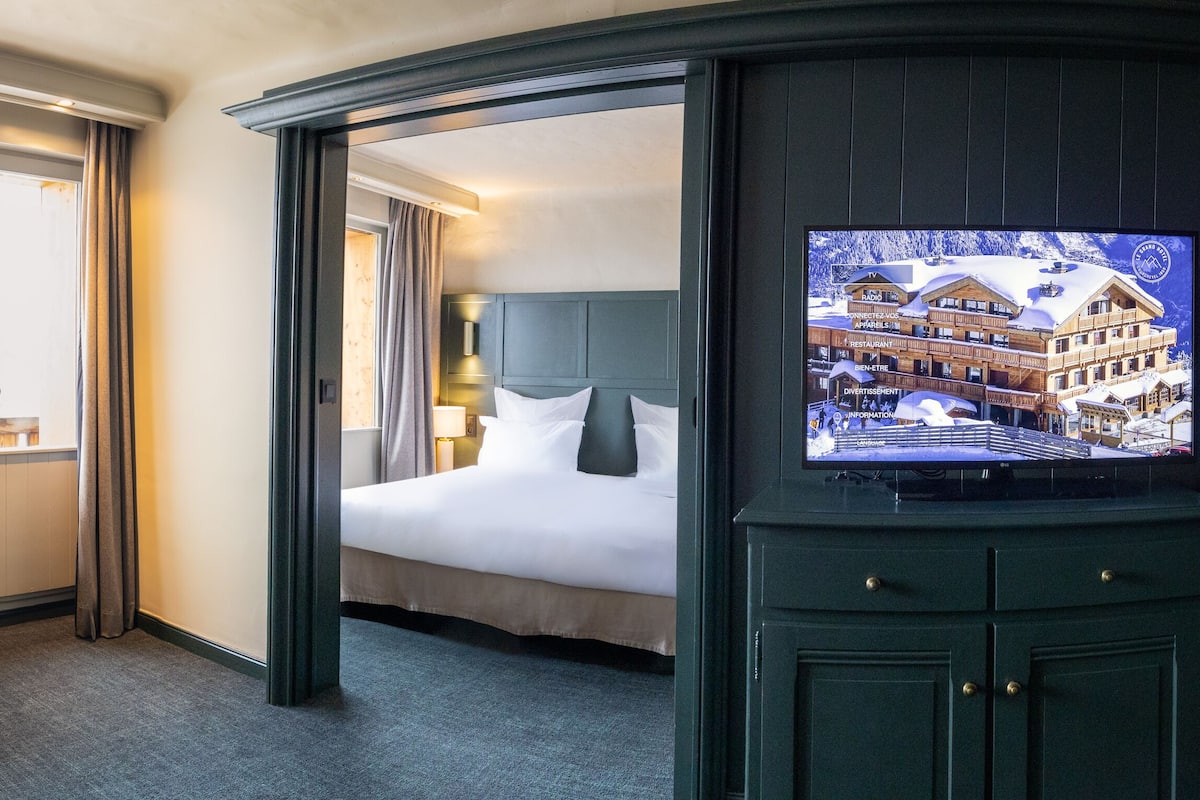 A hotel room with a bed, a desk, a chair, a TV, and a view of a building through the window.