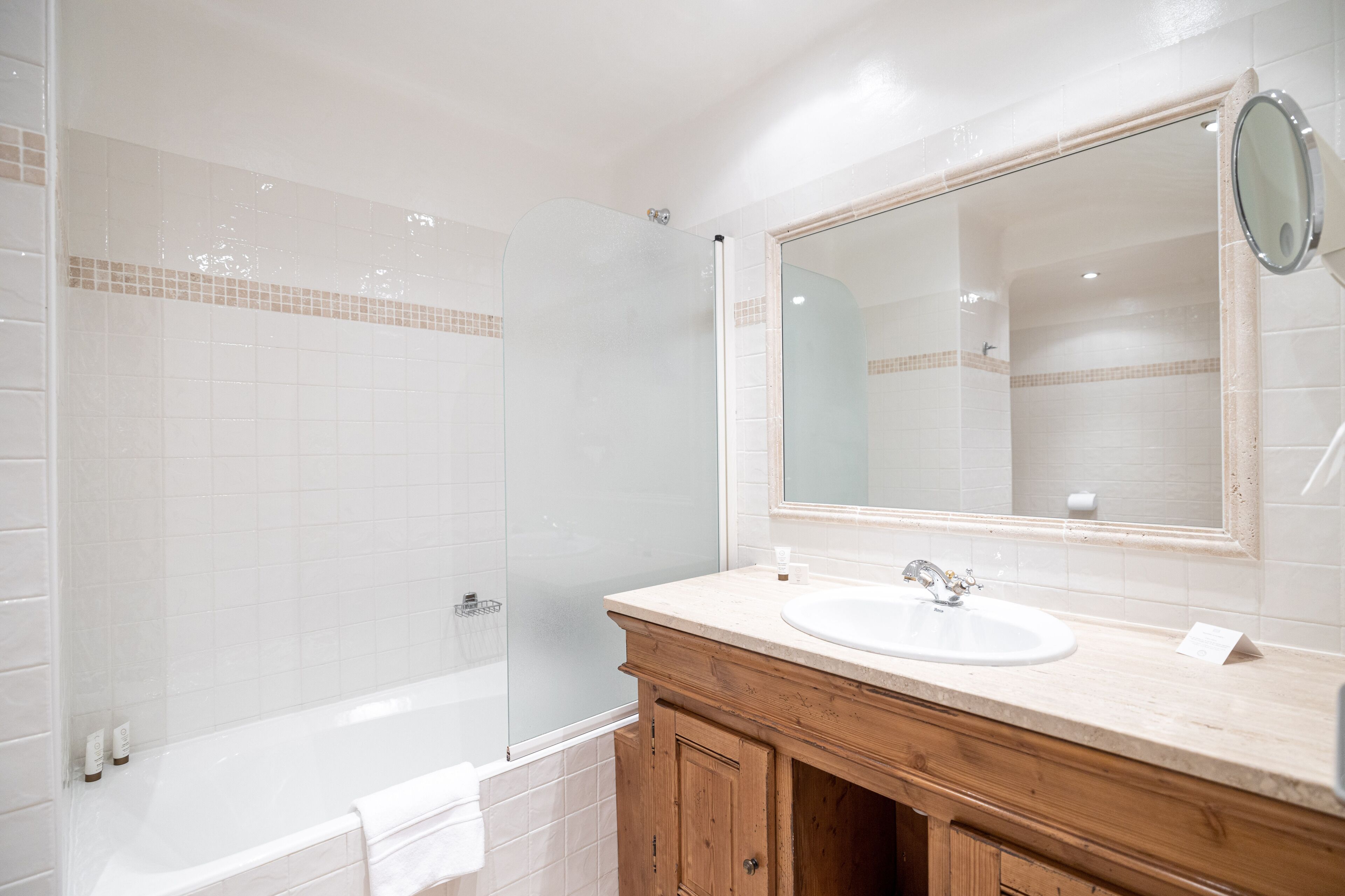 A bathroom with a glass-enclosed shower, a white bathtub, a wooden vanity with a sink, and a large mirror.