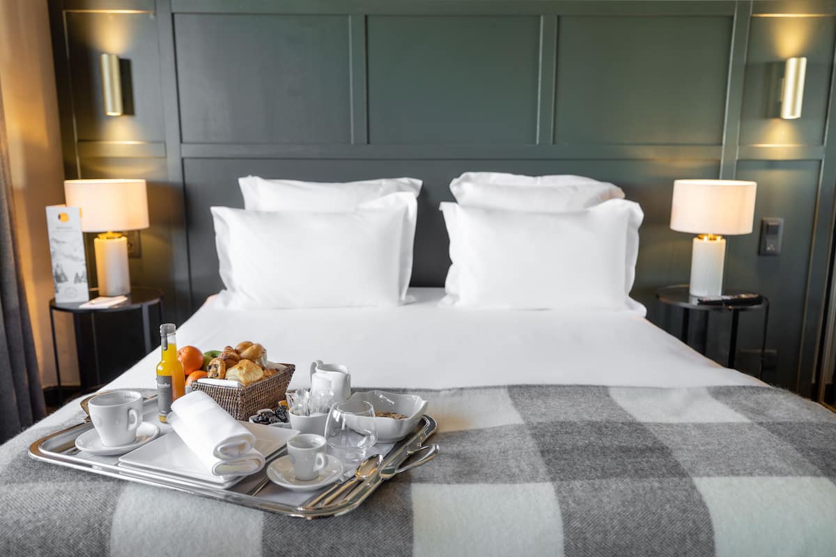 A neatly made bed with white linens, a tray with breakfast items, and two bedside lamps.