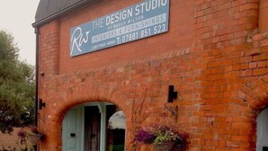 Un bâtiment en briques sur lequel on peut lire l’enseigne « The Design Studio », conçu par Roger Wilson, avec des chaises en osier et des plantes en pot disposées à l’extérieur.