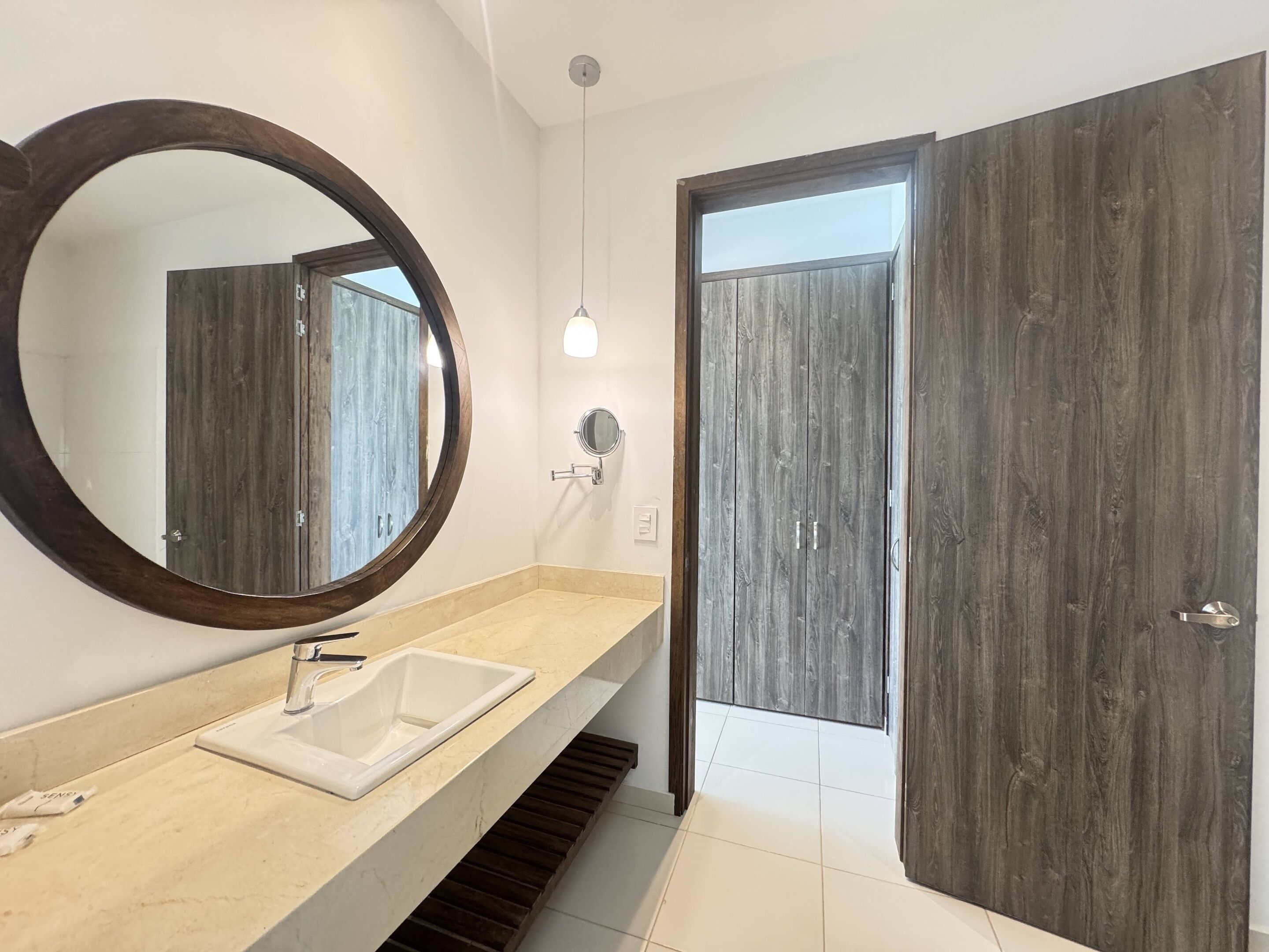 A modern bathroom with a large mirror, a sink, and a wooden door.
