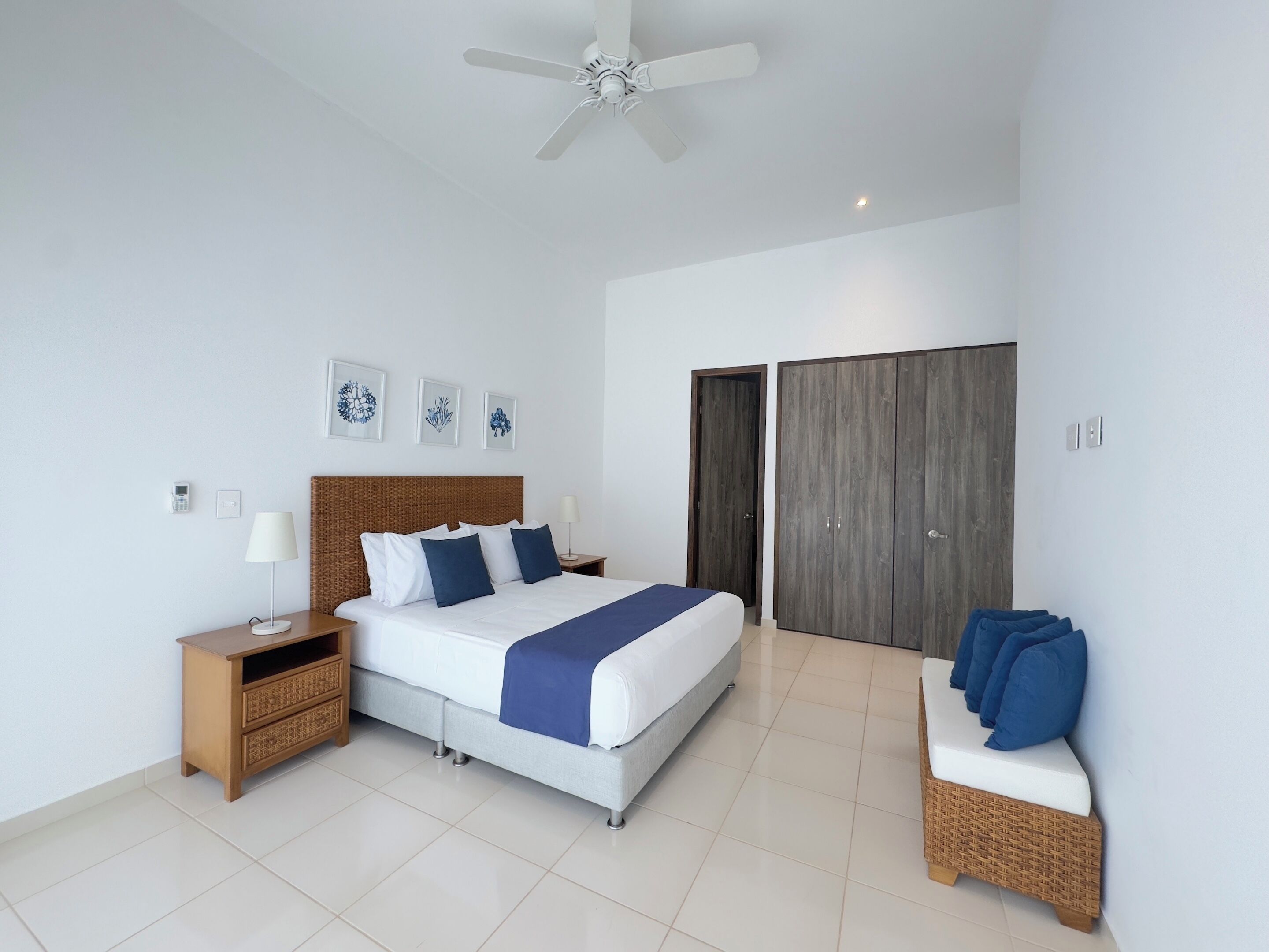 Une chambre à coucher moderne avec un grand lit, un ventilateur de plafond, une armoire et un petit coin salon.