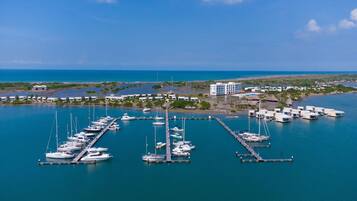 An aerial view of a marina with multiple boats docked, a large building, and a clear view of the ocean.