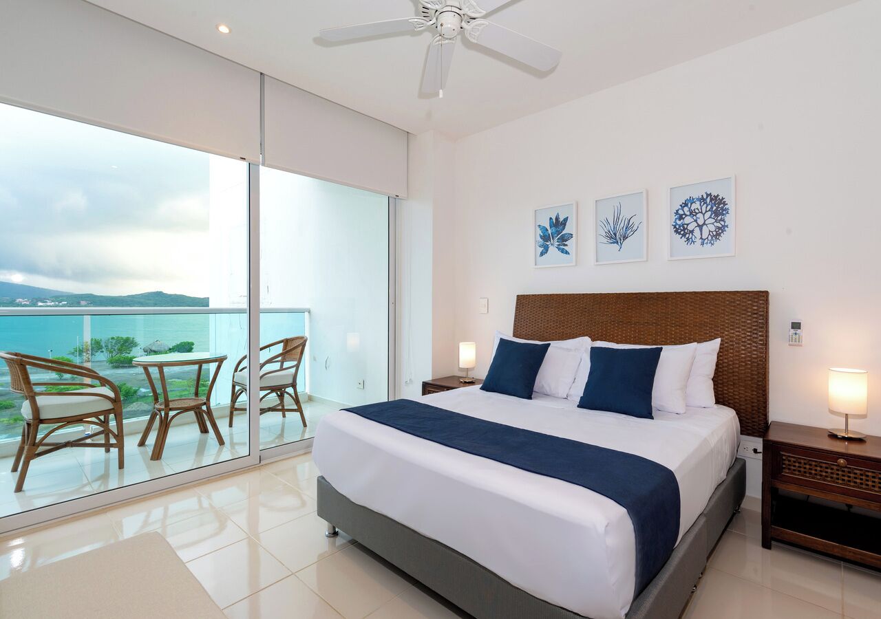 A bedroom with a large bed, a balcony with chairs, and artwork on the wall.