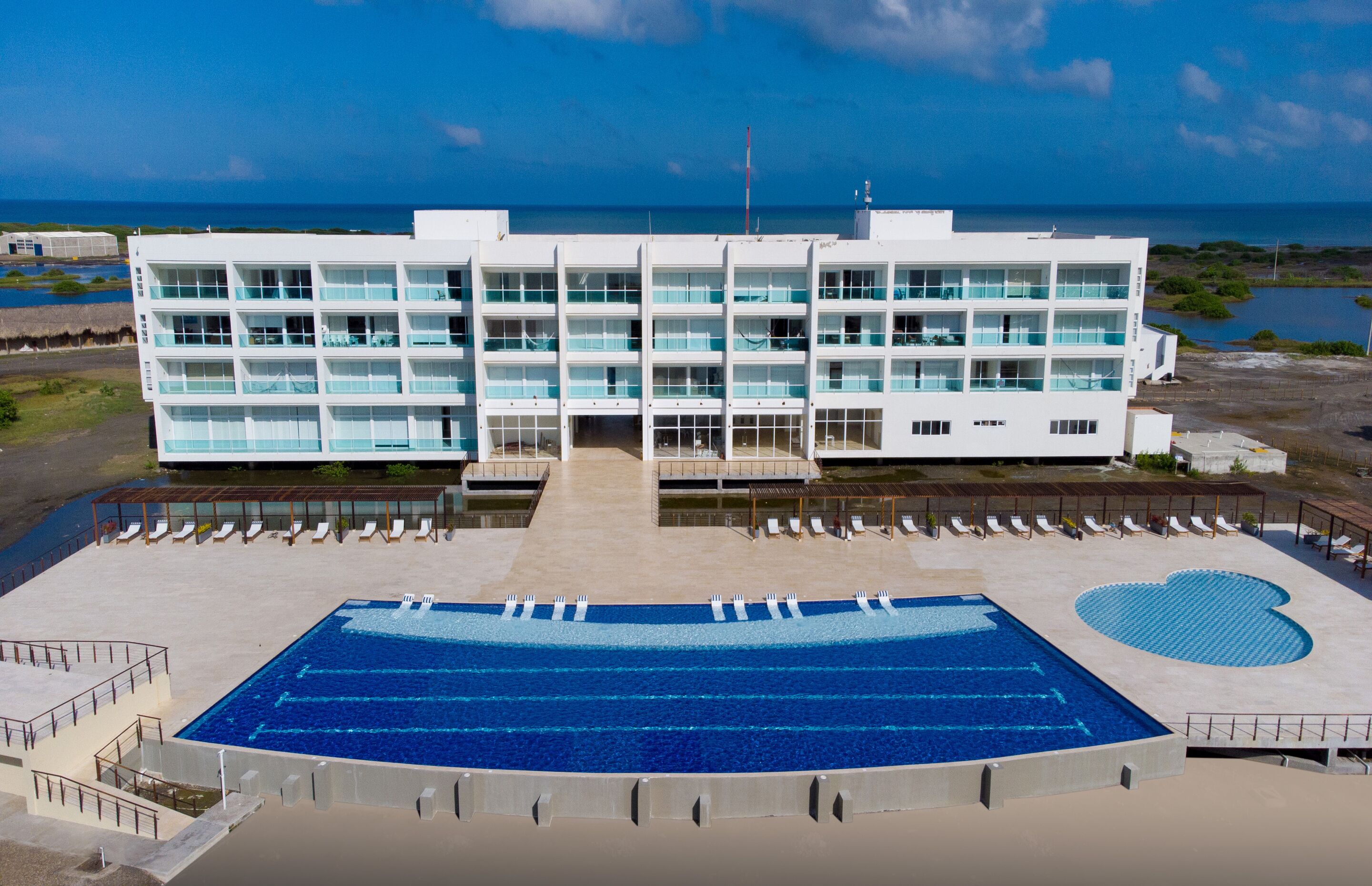 A modern hotel with a large swimming pool, multiple balconies, and a view of the ocean.