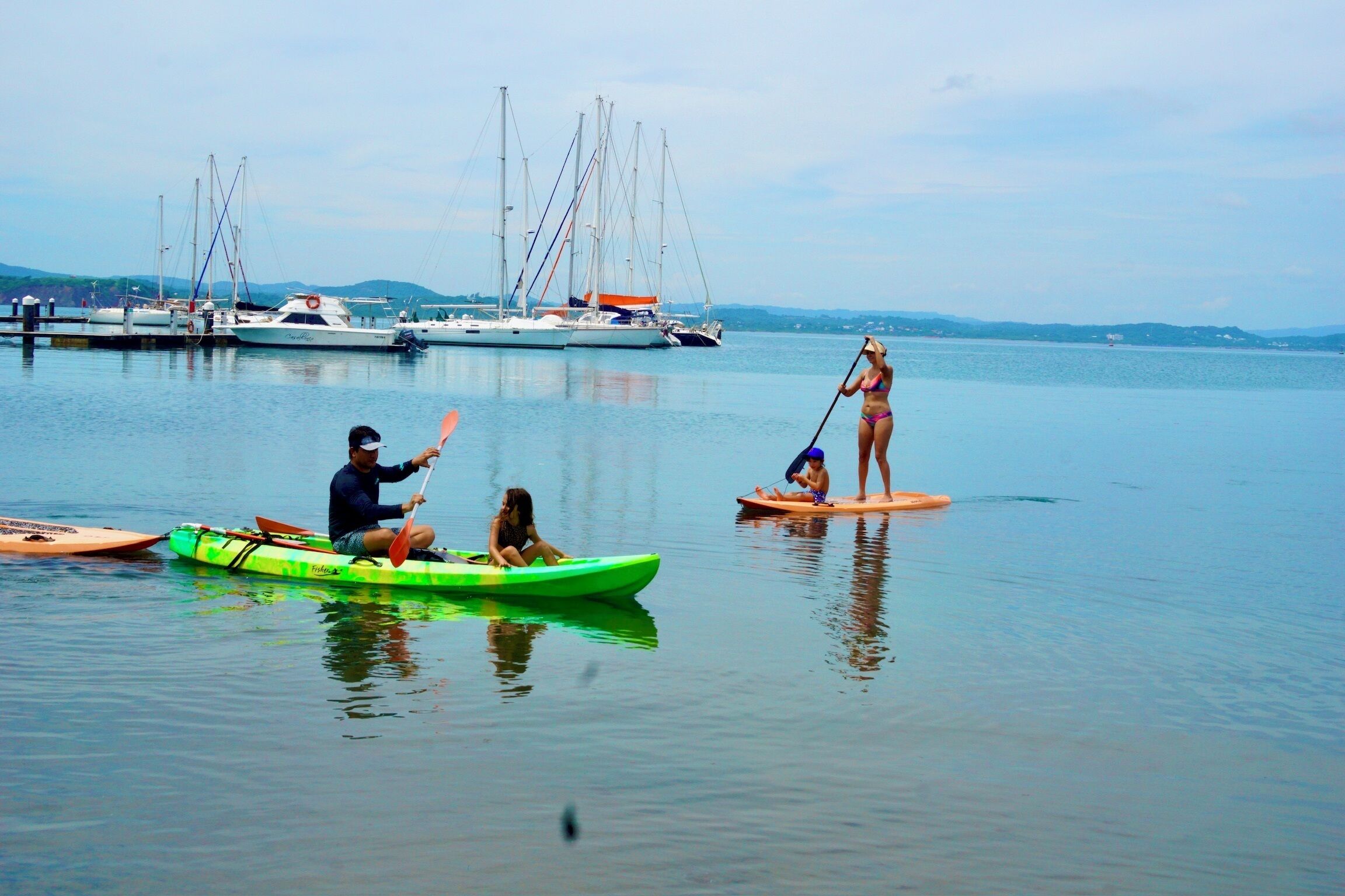 Un puerto tranquilo con varias embarcaciones, incluyendo un kayak verde y una tabla de remo.