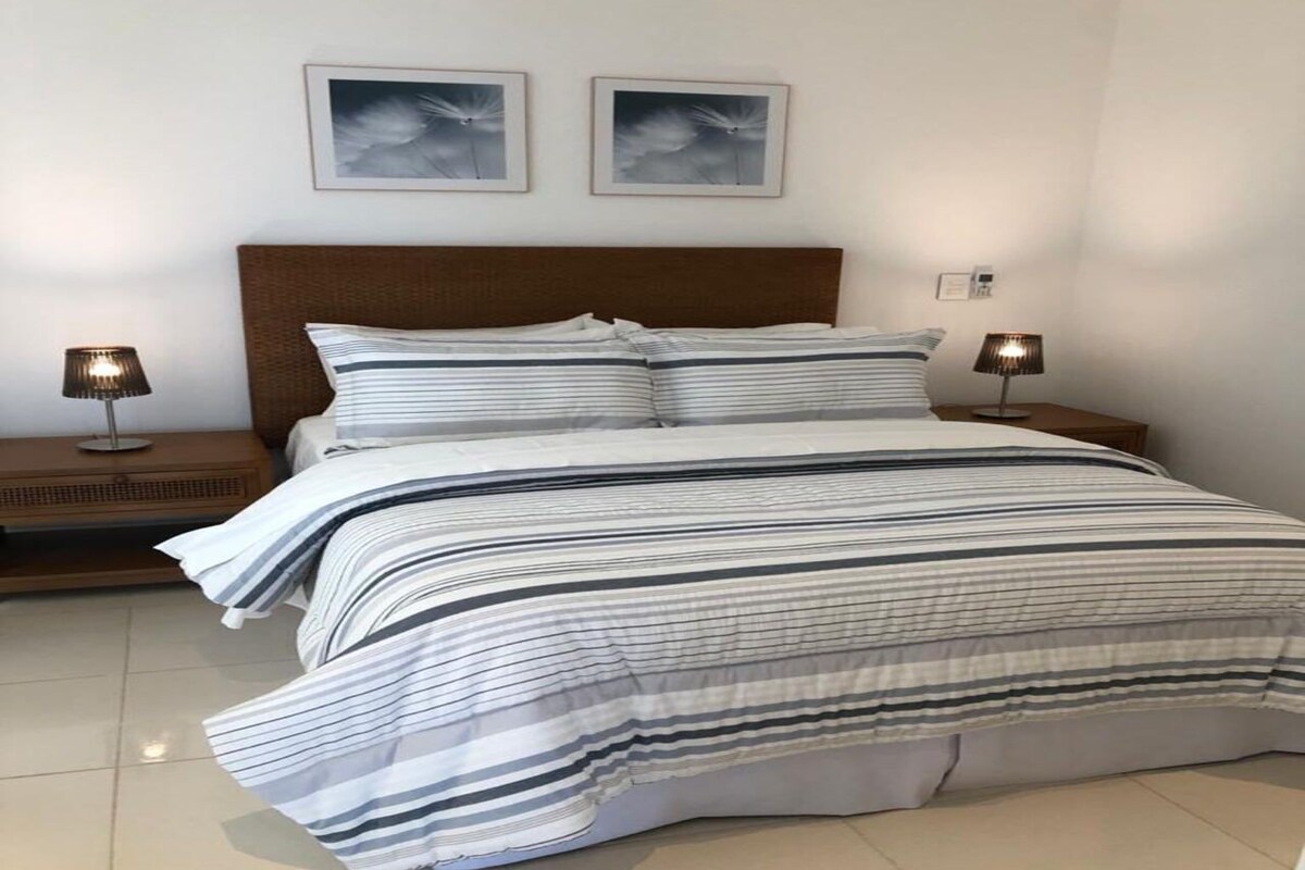 Una cama con ropa de cama a rayas, dos lámparas de noche y dos cuadros en la pared.