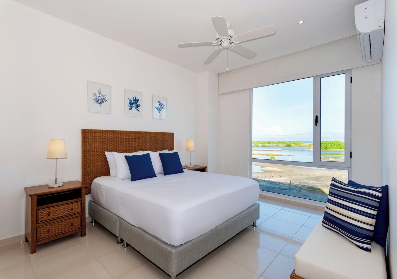 A modern hotel room with a large bed, a ceiling fan, a view to the outside, and a balcony.