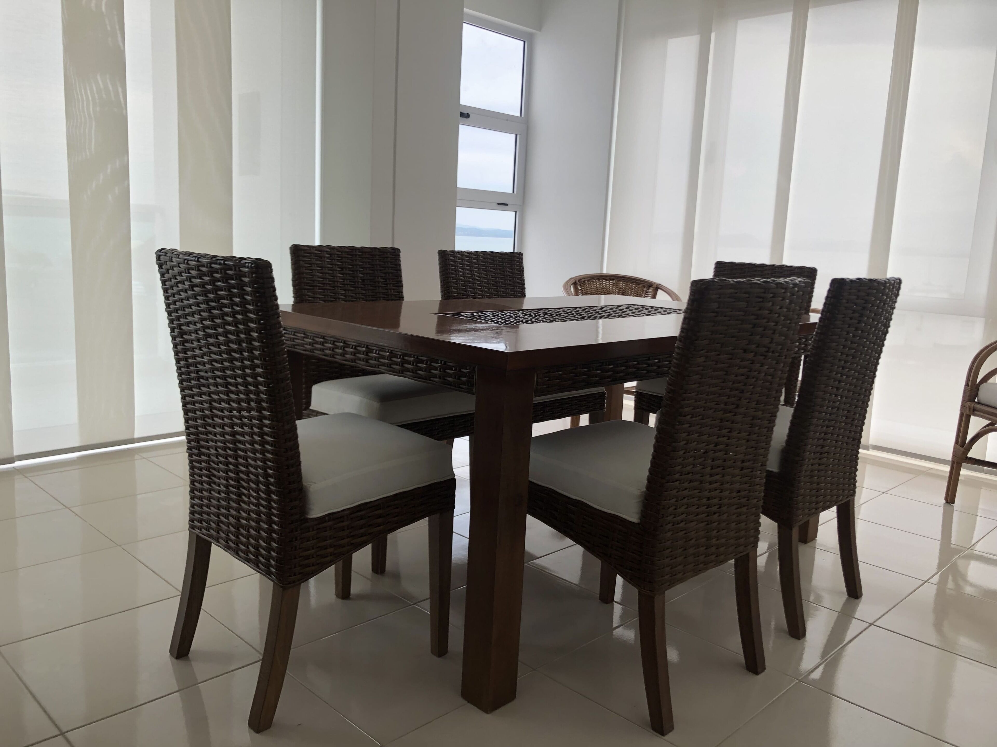 Un coin repas avec une table ronde et six chaises en osier dotées de coussins.