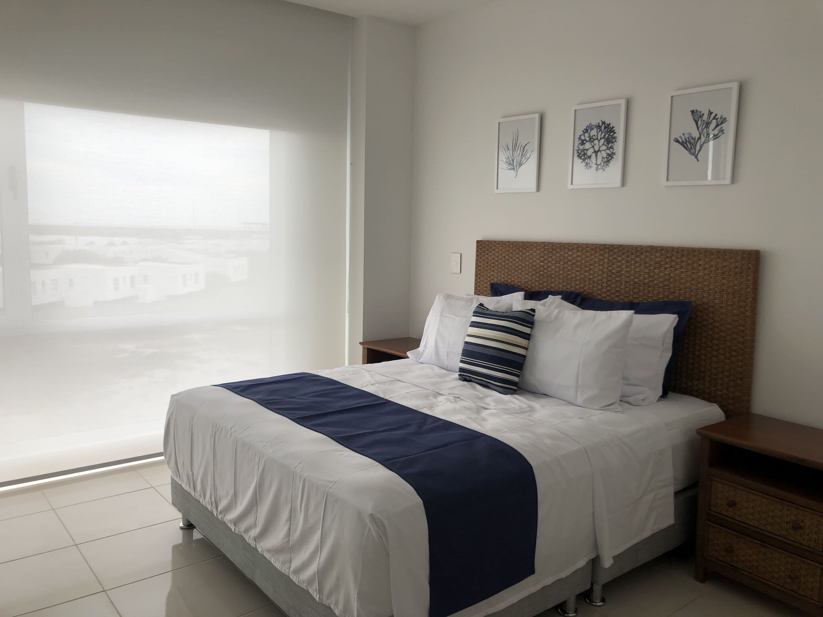 A hotel room with a large bed, a wooden headboard, and three framed botanical prints on the wall.
