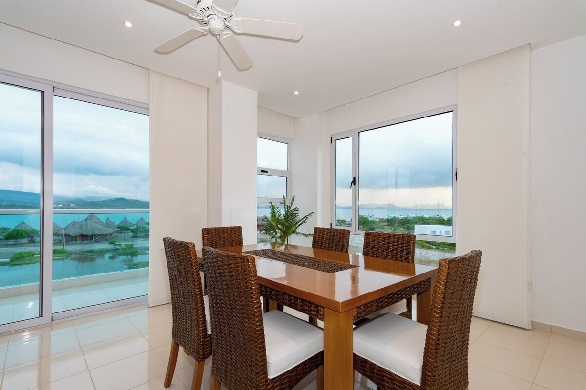 Un comedor con mesa y sillas, ventanas amplias con vistas y un ventilador de techo.