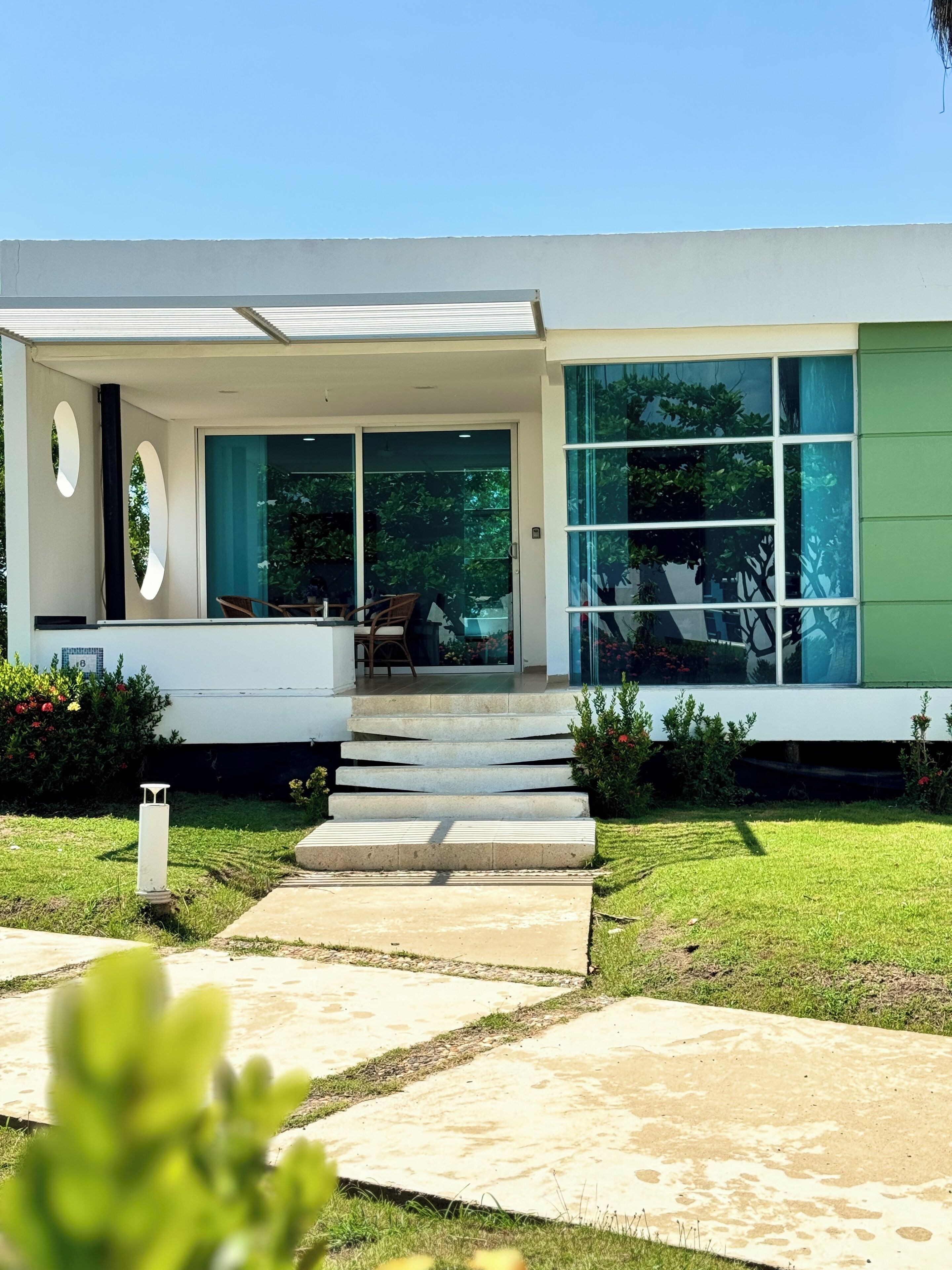 A modern house with a flat roof, large windows, and a front porch with steps leading to the entrance.