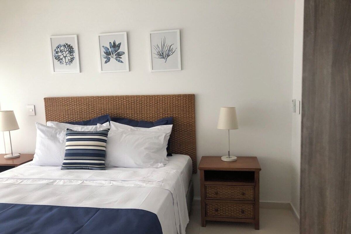 Un dormitorio ordenado con cama, mesitas de noche y decoración en la pared.