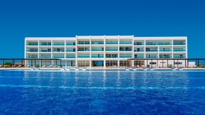 Un hotel moderno con una piscina grande, varios pisos y un cielo azul despejado.