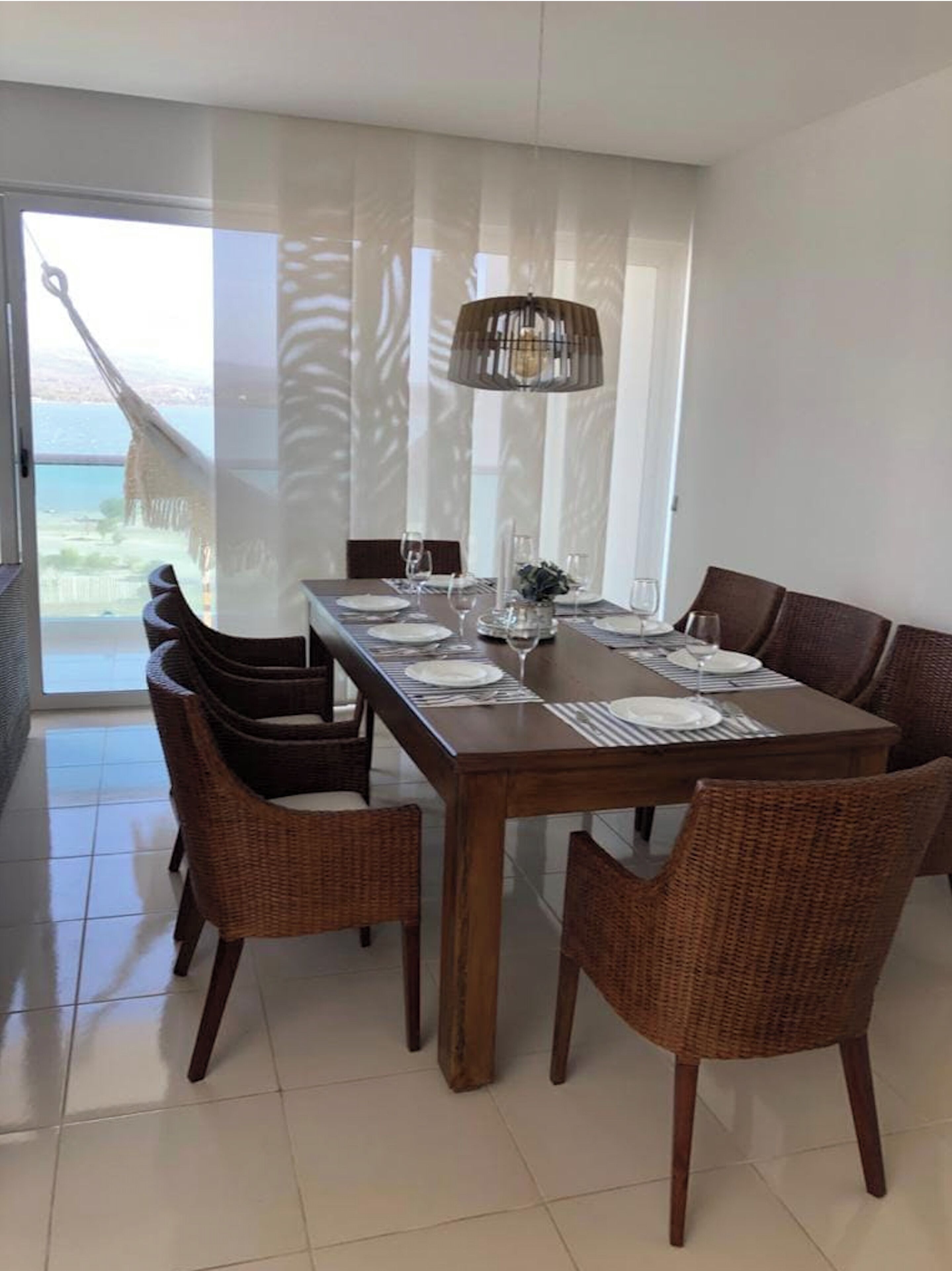 A dining area with a long wooden table set for four, surrounded by wicker chairs.