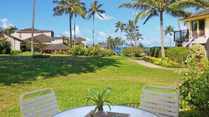A round table with two white chairs, a vase with flowers, and a bird figurine on a tray. - Kahala 712 Ground Floor By Suite Paradise (Koloa)