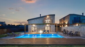 Et moderne hus med swimmingpool, stenvæg og balkon med liggestole.