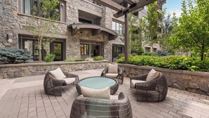 A stone building with a patio area featuring wicker furniture and a glass table. - The Lion Residences E101 (Vail)