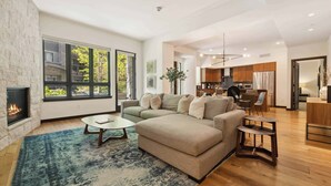 A spacious living room with a fireplace, large windows, and a modern kitchen in the background. - The Lion Residences E101 (Vail)