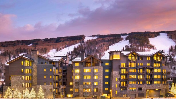 A multi-story hotel with a stone facade, multiple balconies, and a view of a snowy mountain. - The Lion E206 (Vail)