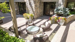 An outdoor patio with wicker furniture, a glass-top table, and potted plants. - The Lion E206 (Vail)