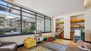A child's playroom with a large window, play mats, a sofa, and a dog. - The Lion E206 (Vail)