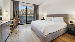 A hotel room with a large bed, a desk with a chair, a small table, and a view of the outdoors through a sliding door. - The Lion Residences W204 (Vail)