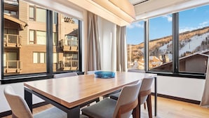 Ein Essbereich mit Holztisch und Stühlen, großen Fenstern mit Blick auf eine verschneite Landschaft und einem Balkon mit Sitzgelegenheit im Freien.