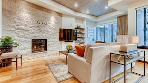 A modern living room with a stone wall, a fireplace, a sofa, a coffee table, and a TV mounted on the wall. - The Lion Residences W101 (Vail)
