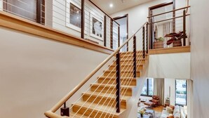 A multi-level interior with a wooden staircase, a living area with a sofa and coffee table, and a view of the outdoors. - The Lion Residences W101 (Vail)