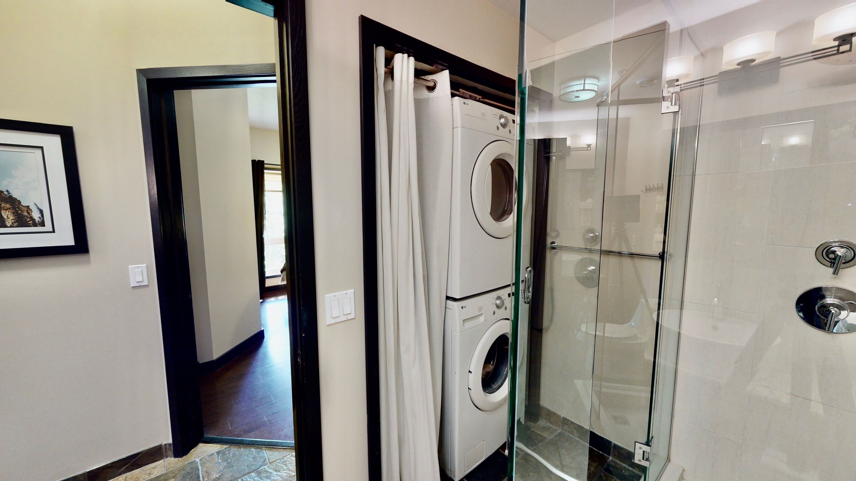 A modern bathroom with a glass-enclosed shower, a built-in washing machine, and a framed picture on the wall.
