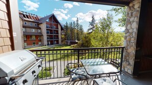 En balkon med grill og bord, med udsigt til en bygning med flere balkoner og en græsplæne.