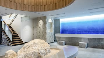 A modern reception area with a wooden reception desk, a stone wall, and a staircase leading to upper floors.