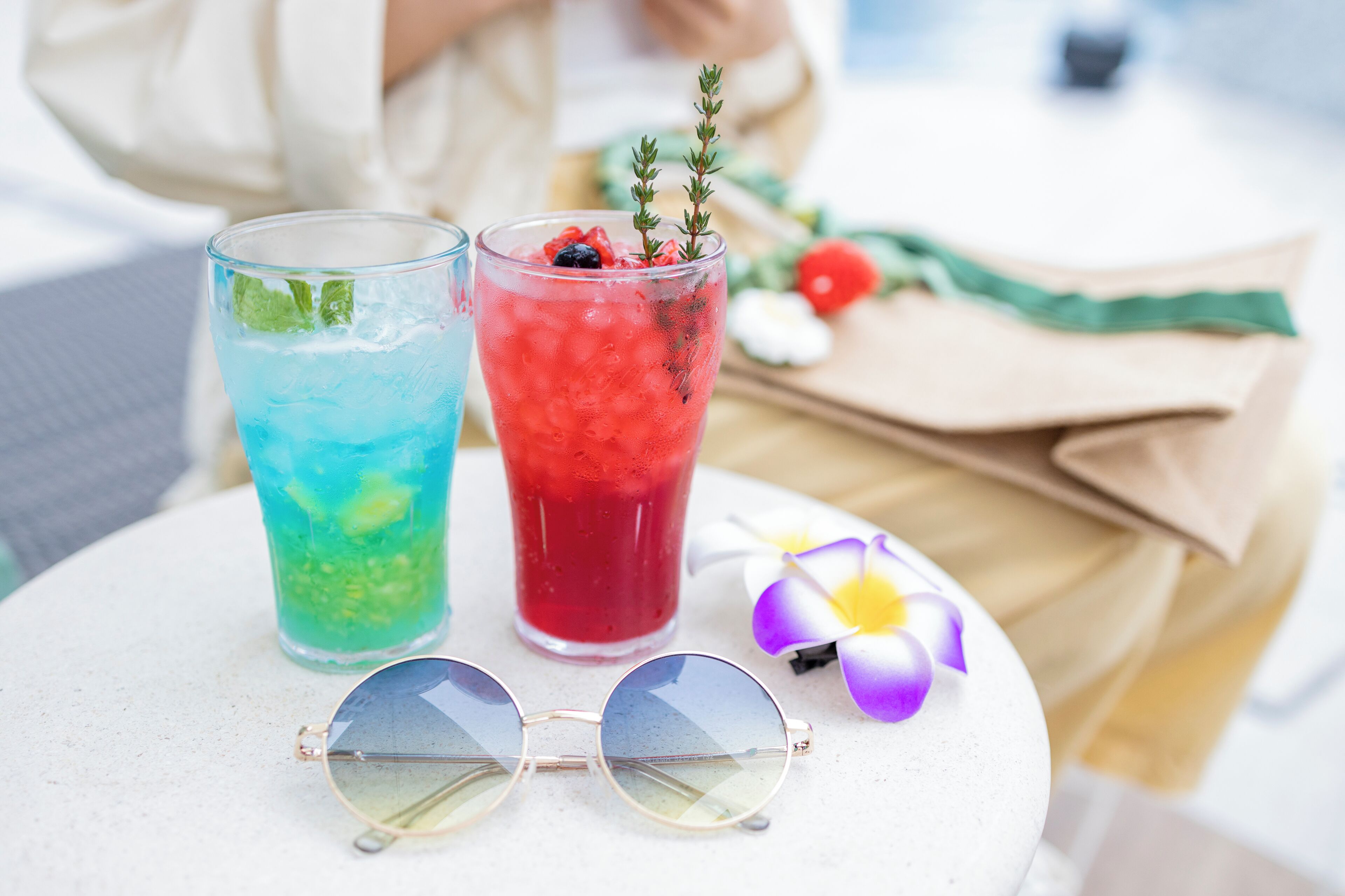 Dos vasos de bebidas heladas sobre una mesa con un par de gafas de sol y una flor.