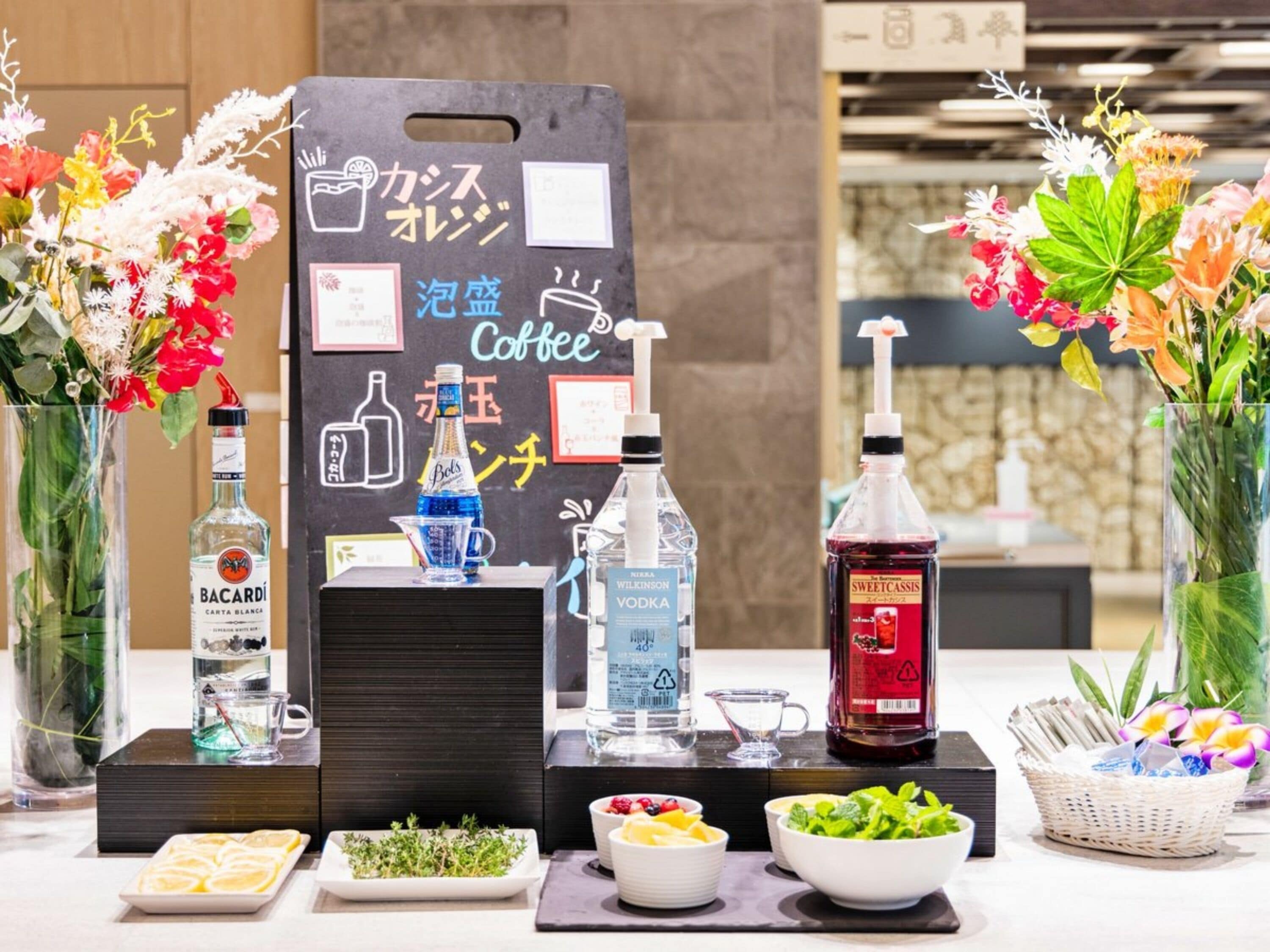 Un espace bar avec un menu écrit à la craie, différentes bouteilles d’alcool et des fleurs fraîches.