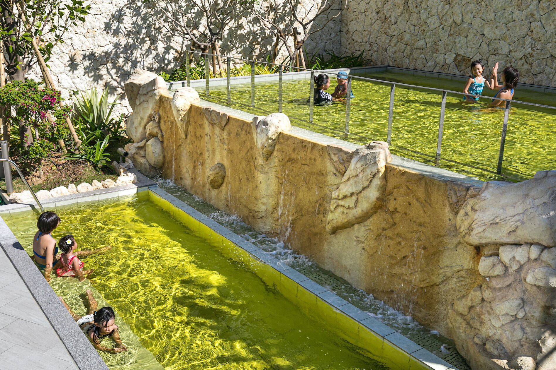 Une piscine avec un mur en pierre et une zone herbeuse.
