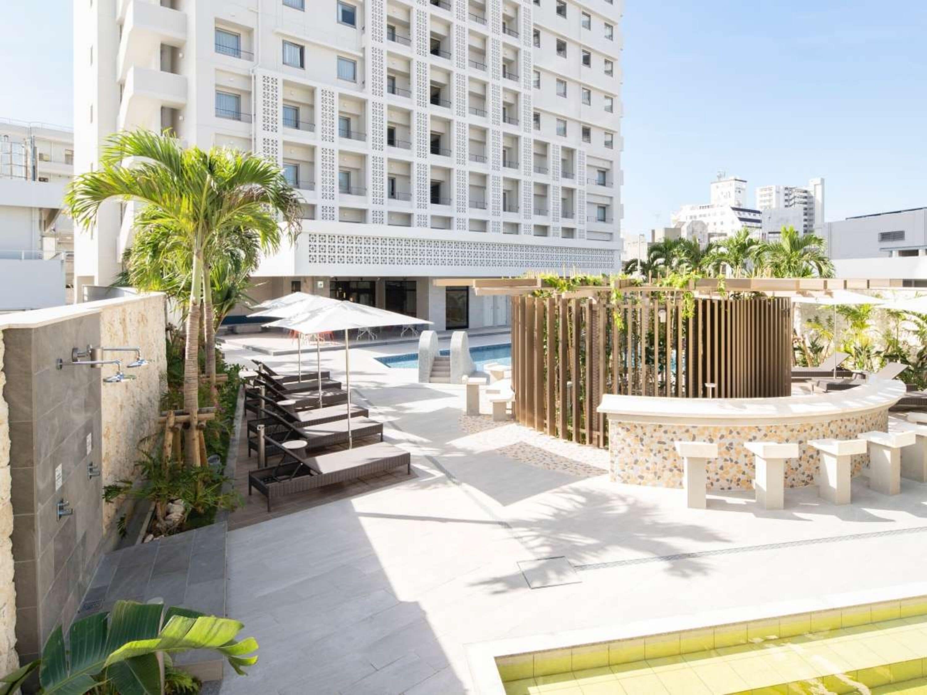 A rooftop pool area with lounge chairs, a water feature, and a view of a high-rise building.