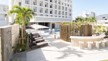 A rooftop pool area with lounge chairs, a water feature, and a view of a high-rise building.
