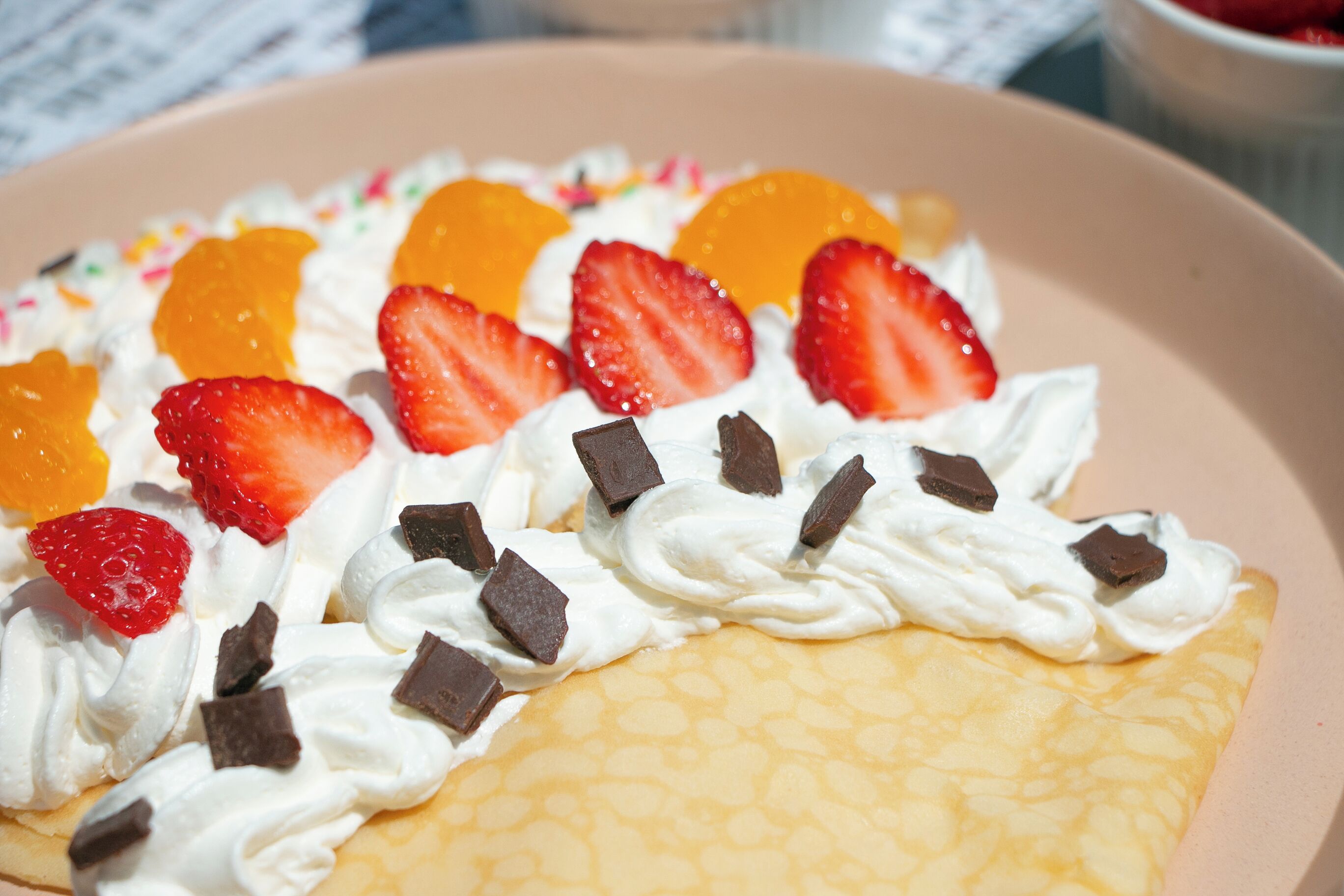 Een dessert met slagroom, aardbeien en stukjes chocolade op een pannenkoek.