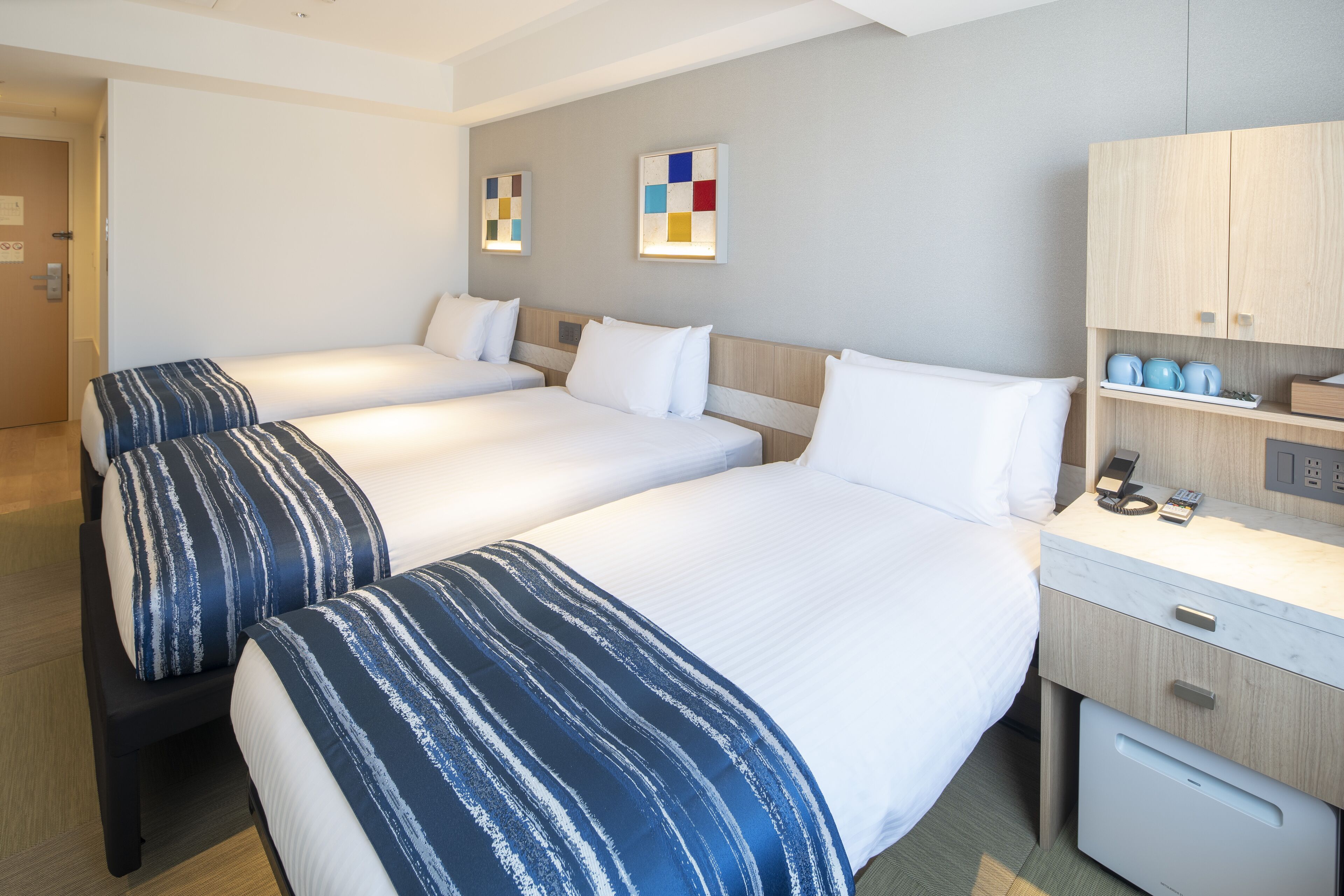 A hotel room with three beds, a desk with a phone, and a cabinet with toiletries.