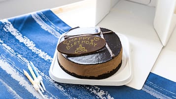 Un pastel de chocolate con glaseado que dice 'Happy Birthday' sobre un pedestal blanco sobre un mantel azul y blanco a rayas.