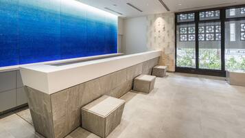 A reception area with a modern design, featuring a marble counter, a blue glass wall, and a view of greenery outside.