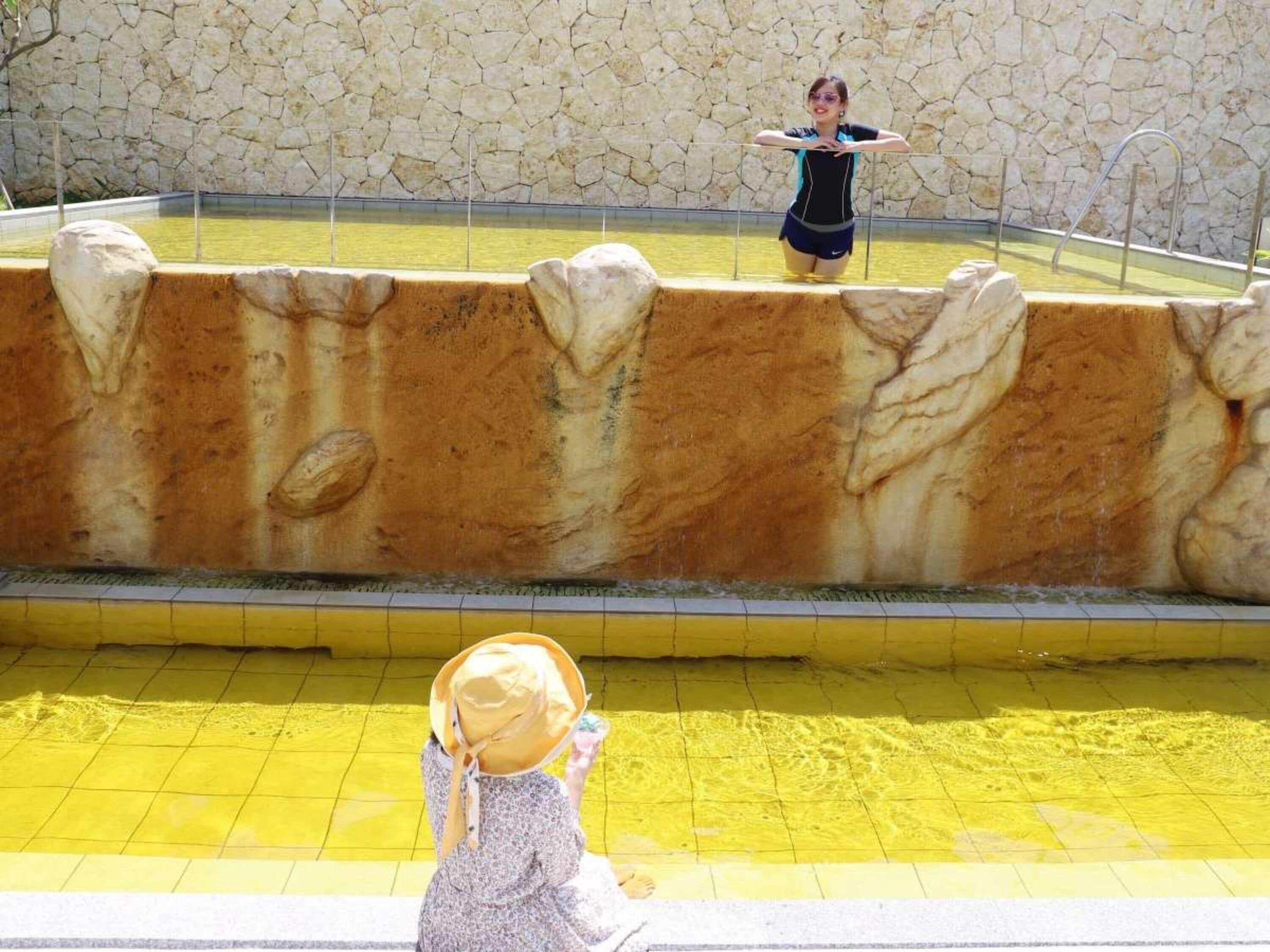 Piscina com parede de pedra e uma pessoa de pé na água.