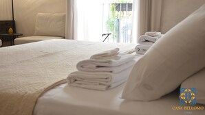 A neatly made bed with folded towels, a bedside table with a lamp, and a view of greenery outside.